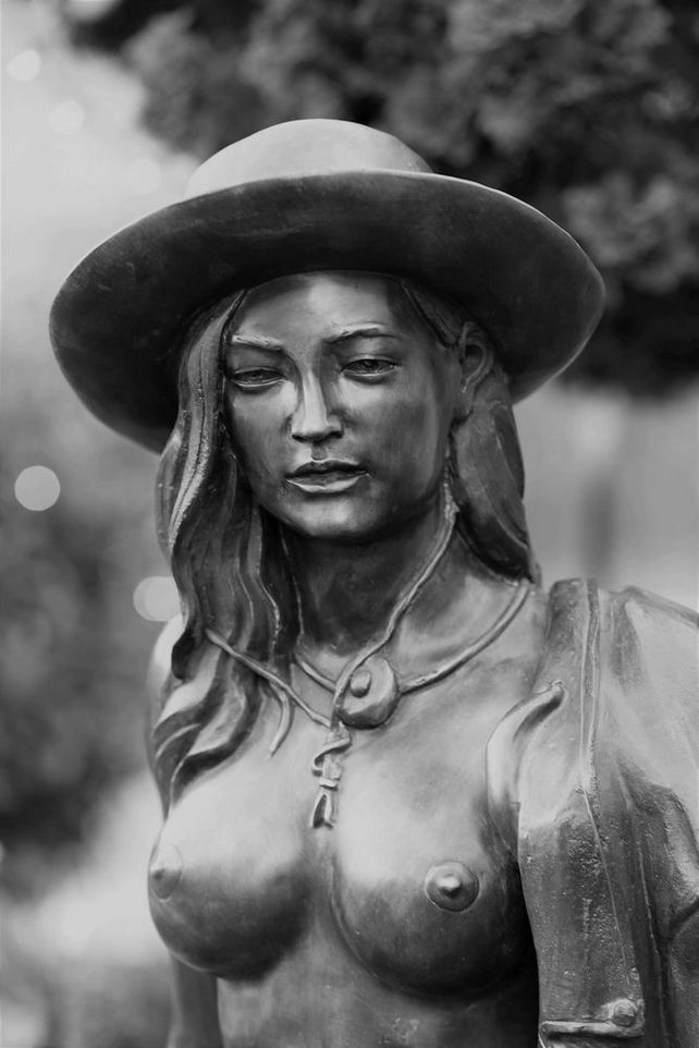 Abbildung einer weiblichen Bronzefigur von stehendem Aktmodell mit Cowboyhut von vorne
