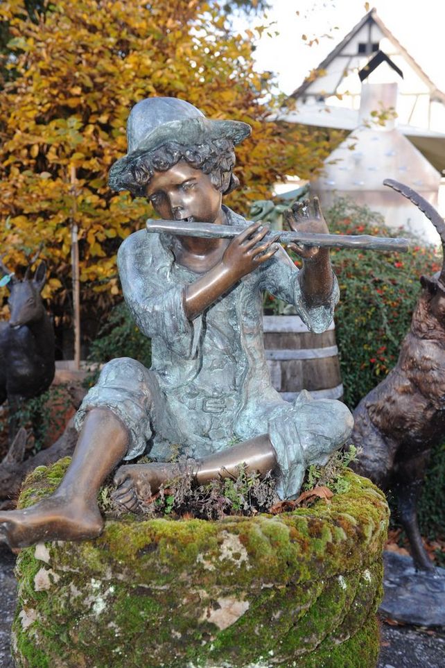 Sitzende Bronzeskulptur eines jugendlichen Flötenspielers mit Hut