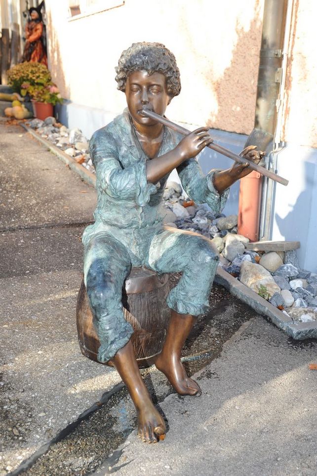 Sitzende Bronzefigur eines jugendlichen Flötenspielers